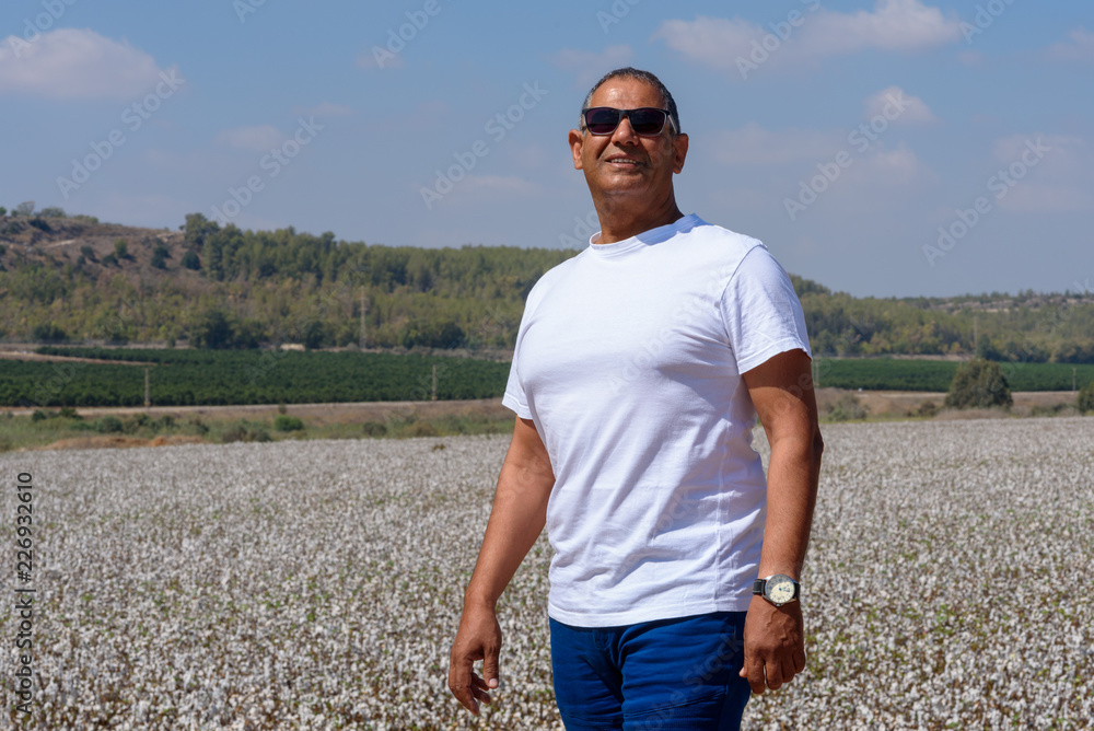 Portrait Of Handsome Active Senior Man Outdoors. Sporty athletic elderly man on background of sky and cotton field. Senior farmer standing in meadow background.