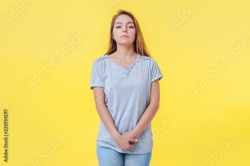 Girl on a yellow background is in a closed pose. Looks with indifference and contempt arrogant