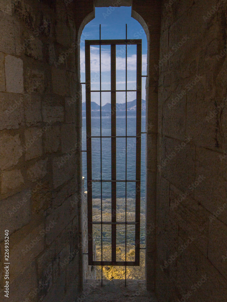 Looking through a narrow window in Lérins Abbey Ruins down at the Mediterranean sea in Cannes, France Looking through a narrow window in Lérins Abbey Ruins down at the Mediterranean sea in Cannes, France