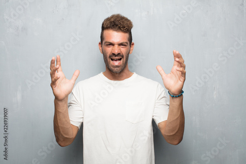 young handsome man looking angry, unhappy and frustrated, gesturing furiously and energically with both hands, feeling upset and annoyed. photo