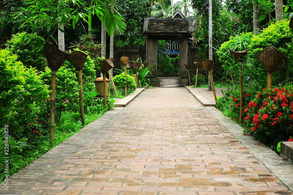 typical south east asian garden with lush vegetation with an old gate and torches along the pavement