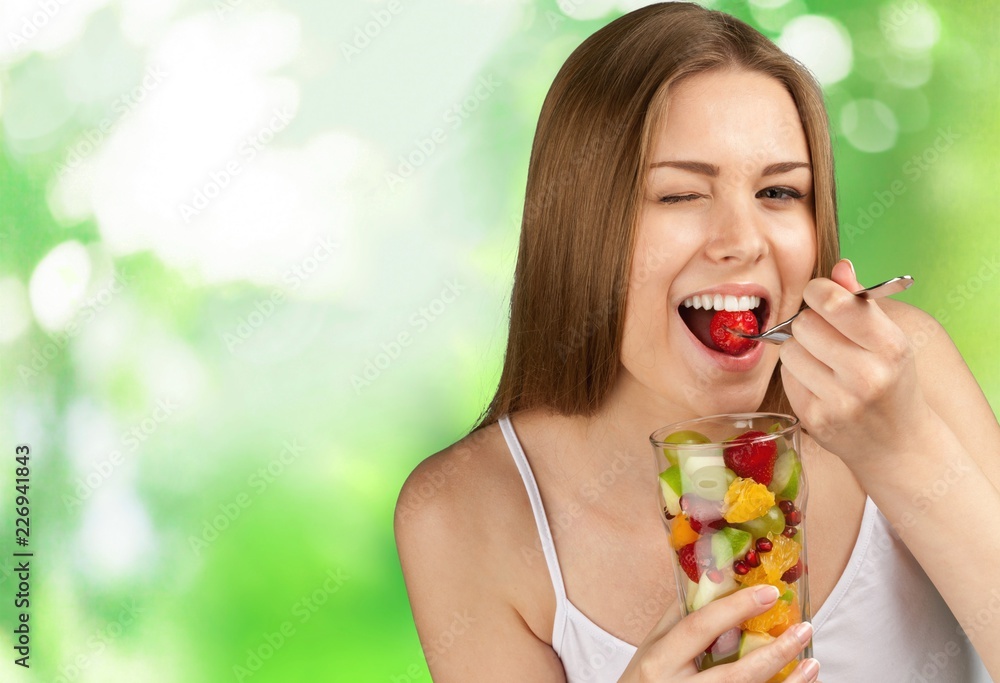 Young woman eating fruits from glass on blurred background Young woman eating fruits from glass on blurred background