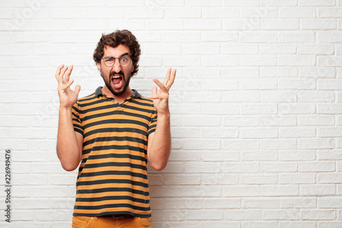 young dumb man looking angry, unhappy and frustrated, gesturing furiously and energically with both hands, feeling upset and annoyed. photo