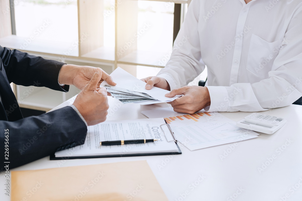 Bribery and corruption concept, bribe in the form of dollar bills, Businessman giving money in the envelope while making deal to agreement a real estate contract and financial corporate Bribery and corruption concept, bribe in the form of dollar bills, Businessman giving money in the envelope while making deal to agreement a real estate contract and financial corporate