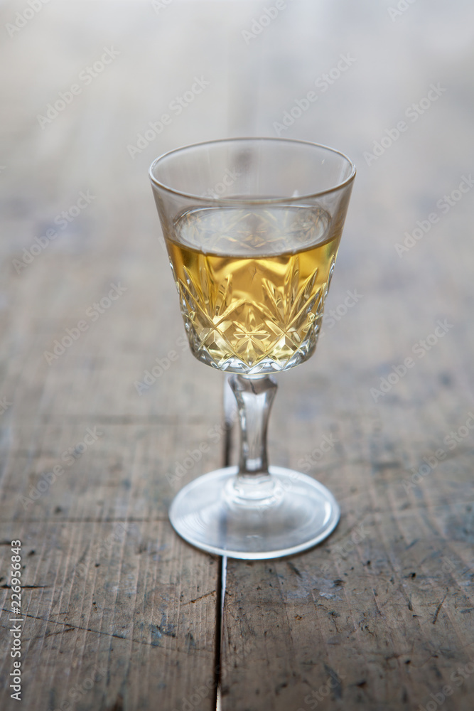 Glass of white wine in a antique glass, placed on a old wooden table.