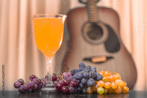 a glass of unfiltered beer on the background of an acoustic guitar with bunches of pink, black and white grapes