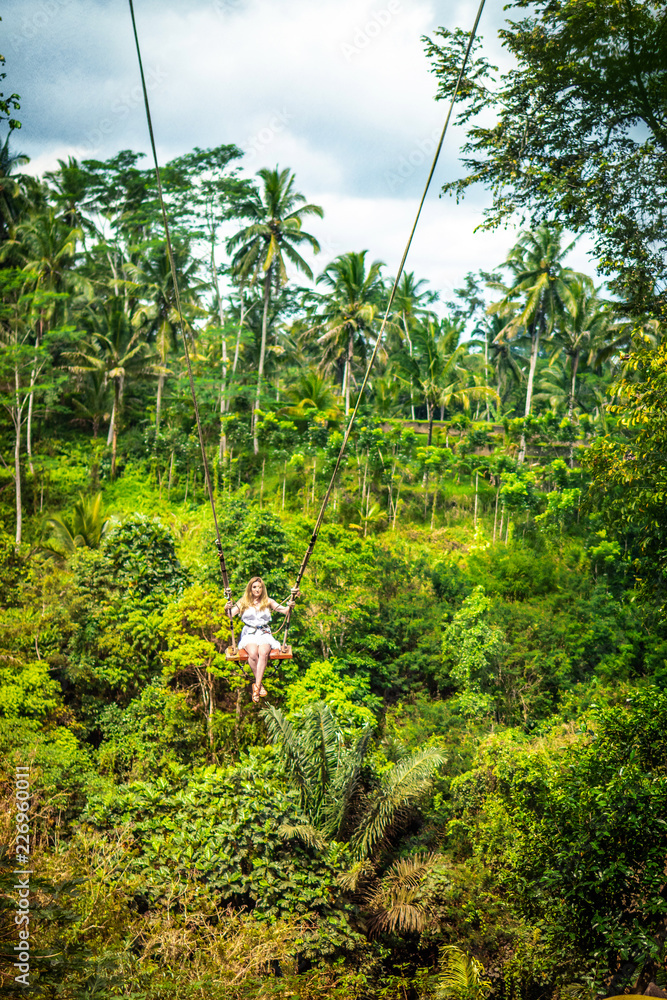 Young tourist woman swinging on the cliff in the jungle rainforest of a tropical Bali island. Young tourist woman swinging on the cliff in the jungle rainforest of a tropical Bali island.
