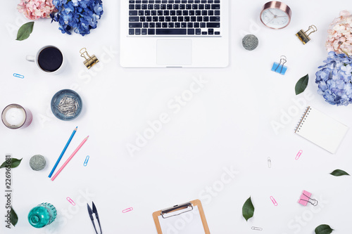 Feminine desk workspace frame with beauty arrangement of bouquet hydrangeas, laptop, clipboard, notebook, pencil and candle on white background. Flat lay, Top view office table desk with copy space. 