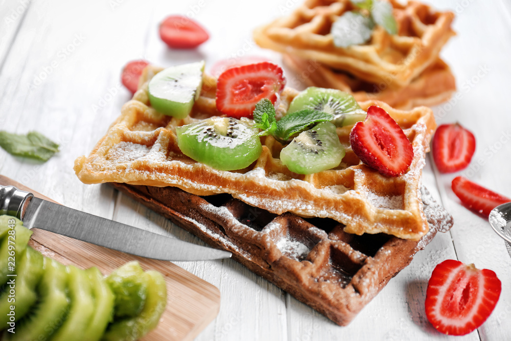 Delicious waffles with kiwi slices and strawberry on white wooden table