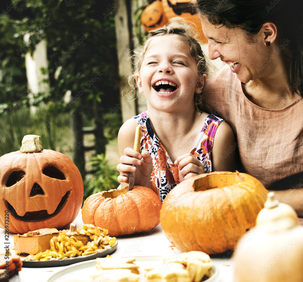 Fototapeta premium Young cheerful girl carving pumpkins with her mom