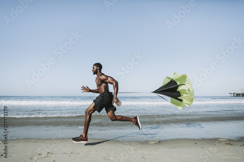 Fit man with a running parachute at the beach