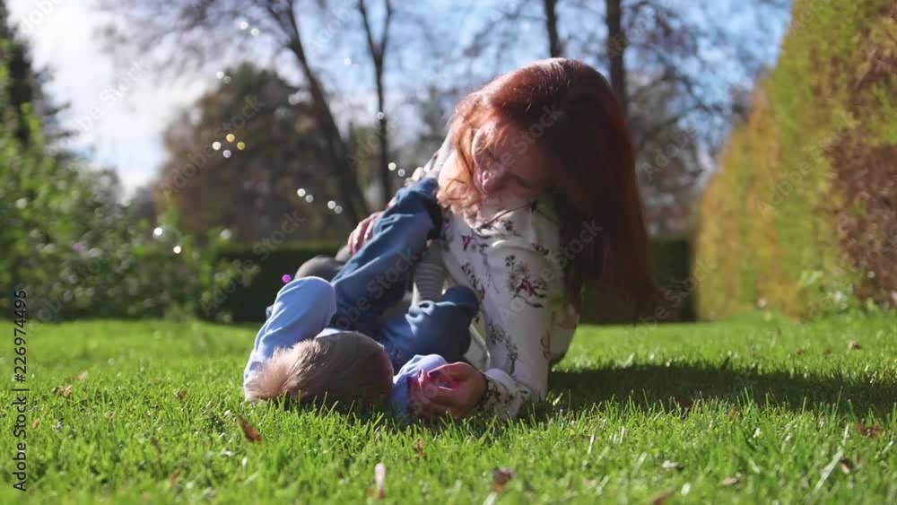 Happy family resting on the lawn.Mother with tenderness and love hugs her child, the son laughs. Happy childhood Happy family resting on the lawn.Mother with tenderness and love hugs her child, the son laughs. Happy childhood