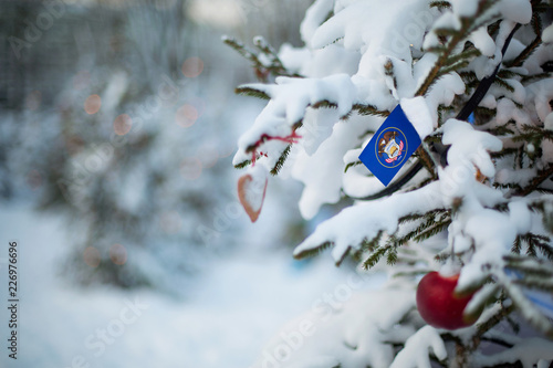 Utah state flag. Christmas background outdoor. Christmas tree covered with snow and decorations and Utah flag.  New Year / Christmas holiday greeting card. © theartofpics