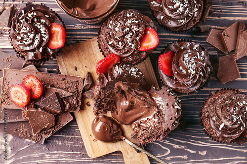 Tasty cupcakes with strawberry and pieces of chocolate bar on wooden table