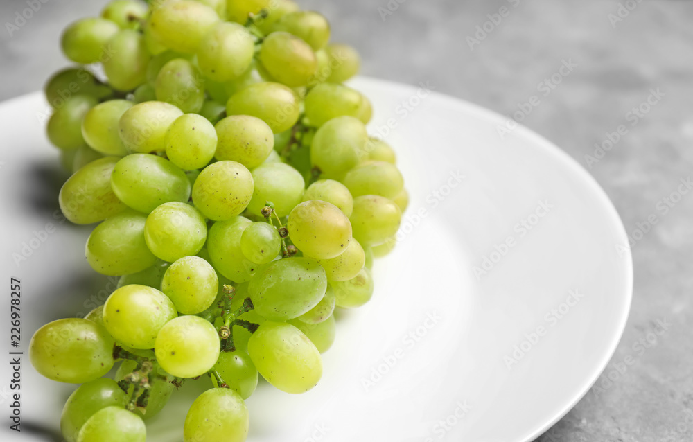 Plate with ripe juicy grapes on grey table, closeup