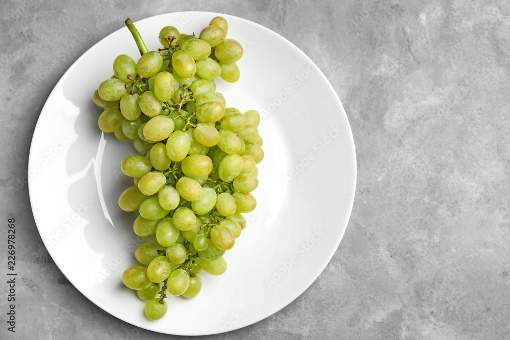 Plate with ripe juicy grapes on grey table Plate with ripe juicy grapes on grey table