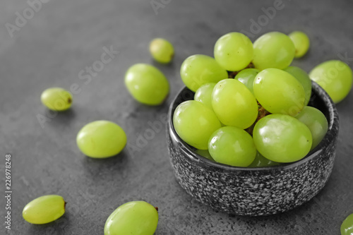 Bowl with ripe juicy grapes on grey table