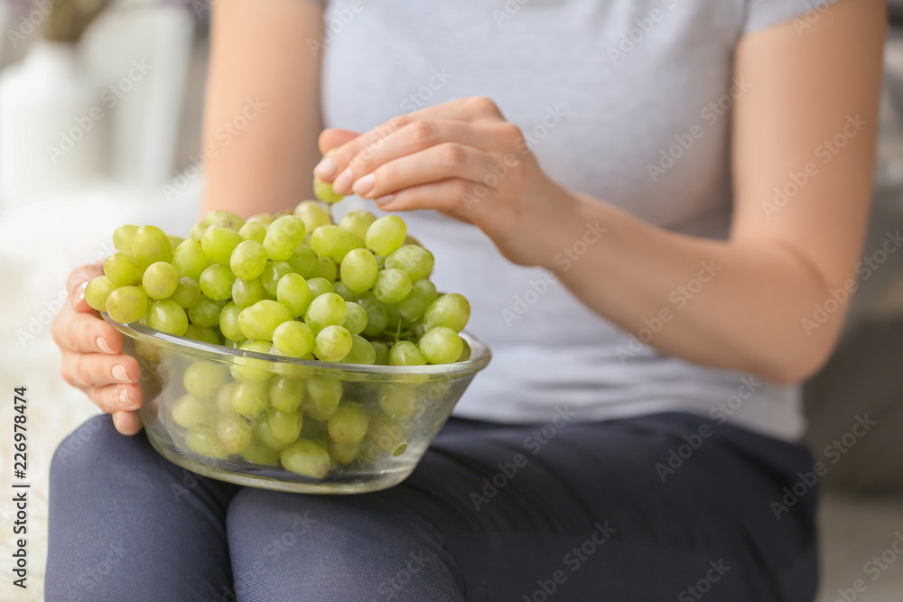 Fototapeta premium Woman holding glass bowl with ripe juicy grapes, closeup