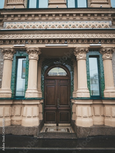 The facade of the historic old building with a large wooden door, columns and green brick