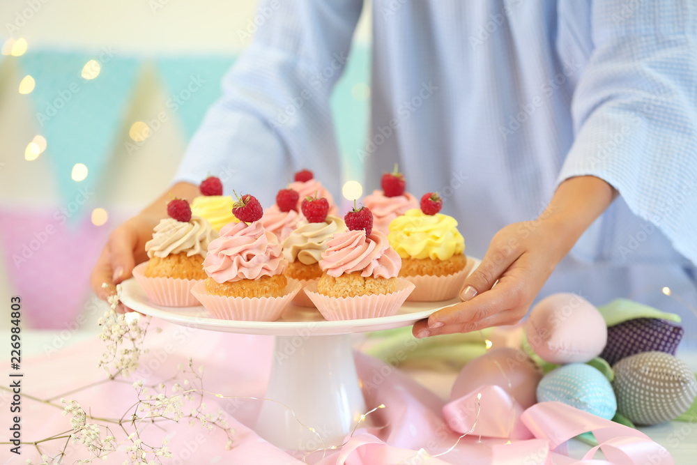 Woman putting stand with delicious cupcakes on table, closeup Woman putting stand with delicious cupcakes on table, closeup
