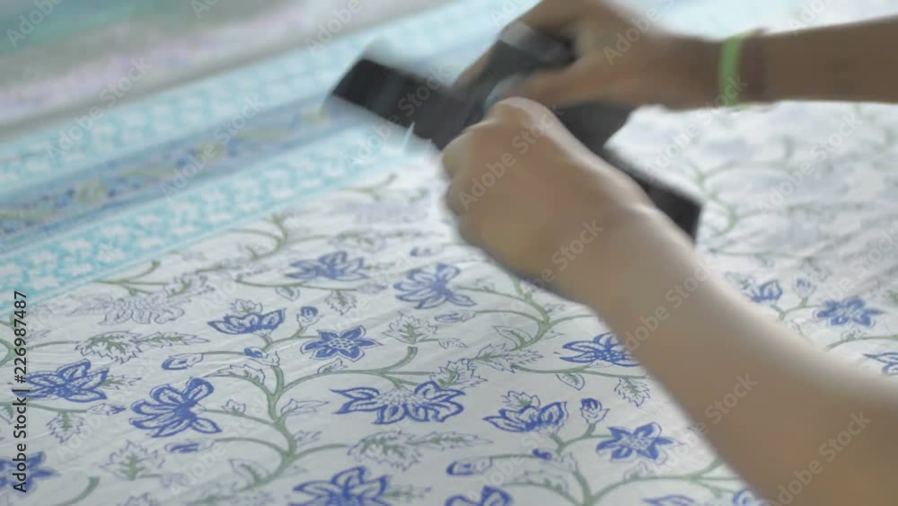 Close up of a hands printing colorful design on a cotton sheet using traditional wood block printing method in textile printing factory
