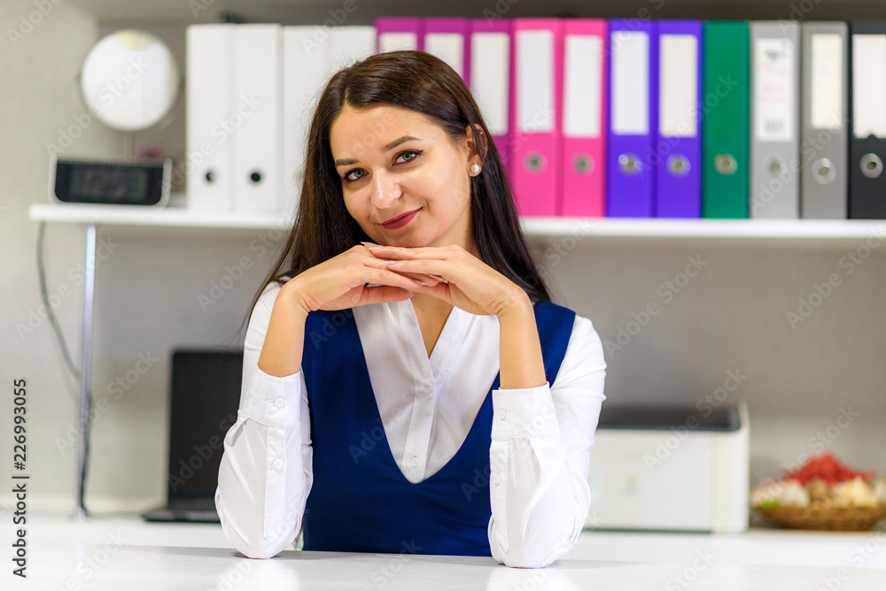 Studio portrait of a beautiful brunette girl in an office sitting at a table. Studio portrait of a beautiful brunette girl in an office sitting at a table.