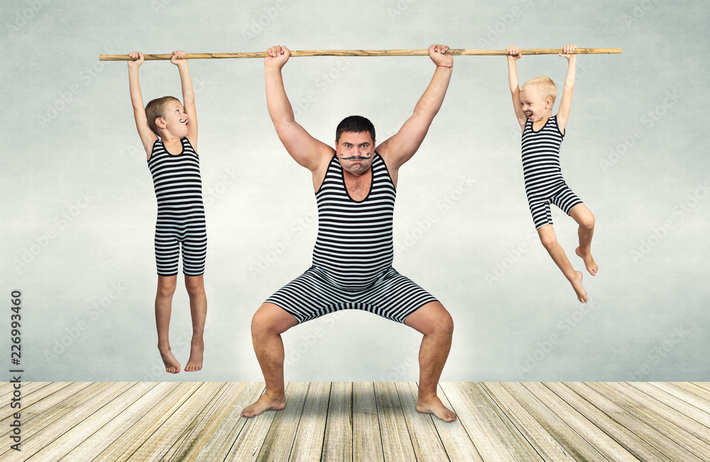 Naklejka premium Family of strongman. The father of two sons in vintage costume of athletes perform strength exercises. Family look.