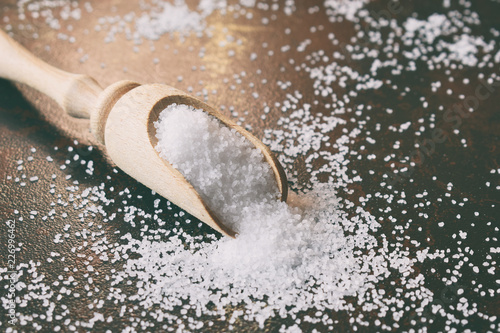 Sea salt, finely ground scattered in wooden spoon on black background.