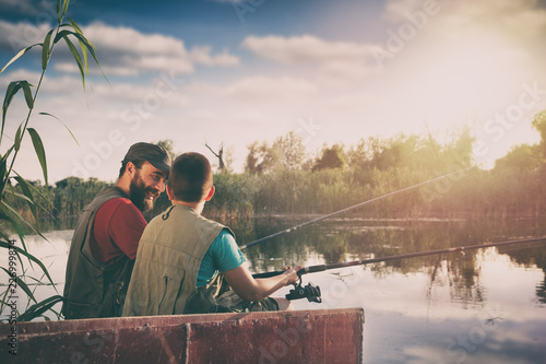 father and son sitting in boat on lake while fishing together