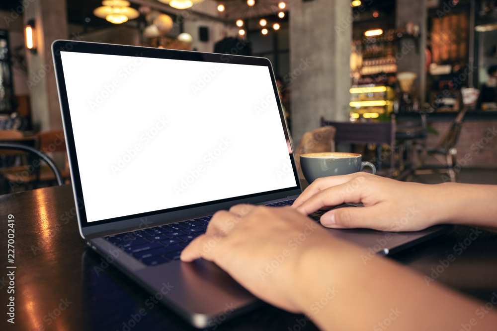 Mockup image of hands using and typing at laptop with blank white desktop screen with coffee cup on wooden table in cafe Mockup image of hands using and typing at laptop with blank white desktop screen with coffee cup on wooden table in cafe