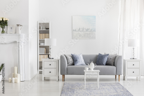 White table on carpet in front of grey settee in apartment interior with painting and lamp. Real photo