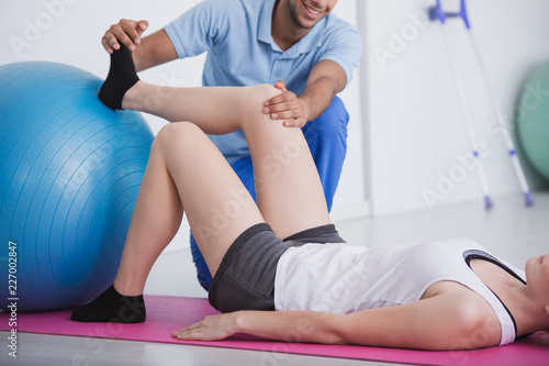 Physiotherapist holding knee and foot of his patient during rehabilitation with a ball