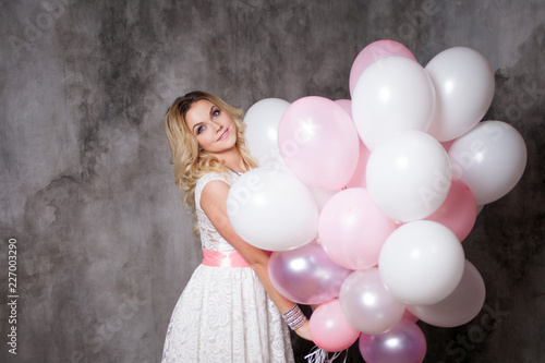 Charming young blonde in a white dress with pink balloons, at the party.