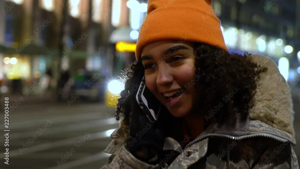 Beautiful mixed race female teenager girl young woman wearing camouflage jacket, an orange beanie hat and talking on cell phone at night with trams by Alexanderplatz Station, Berlin, Germany Beautiful mixed race female teenager girl young woman wearing camouflage jacket, an orange beanie hat and talking on cell phone at night with trams by Alexanderplatz Station, Berlin, Germany