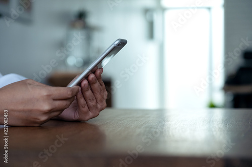 Closeup image a woman's hands holding , using and looking at smart phone on wooden table © Farknot Architect