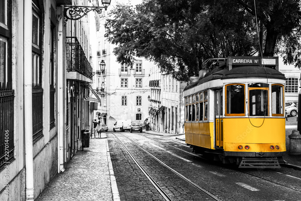 Fototapeta premium Żółty tramwaj na starych ulicach Lizbony, Portugalia, popularna atrakcja turystyczna i miejsce docelowe. Czarno-biały obraz z kolorowym tramwajem.
