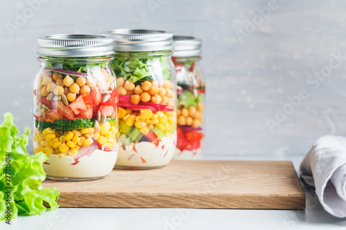 Three glass jars with layering various vegan salads for healthy lunch. The concept of fitness and vegetarian food. Copy space.