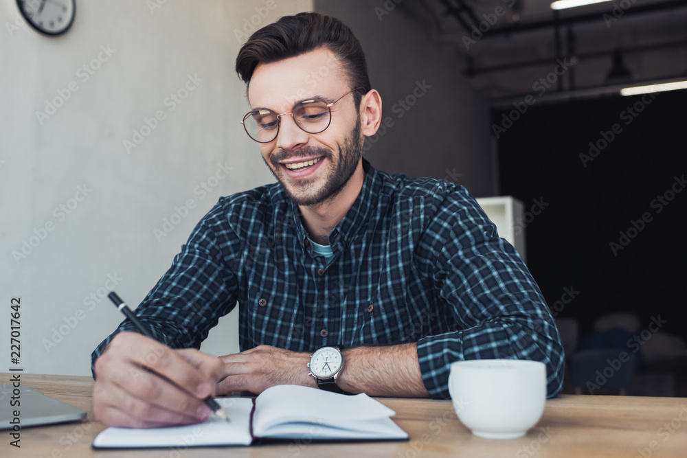 portrait of smiling businessman making notes in notebook at workplace in office portrait of smiling businessman making notes in notebook at workplace in office