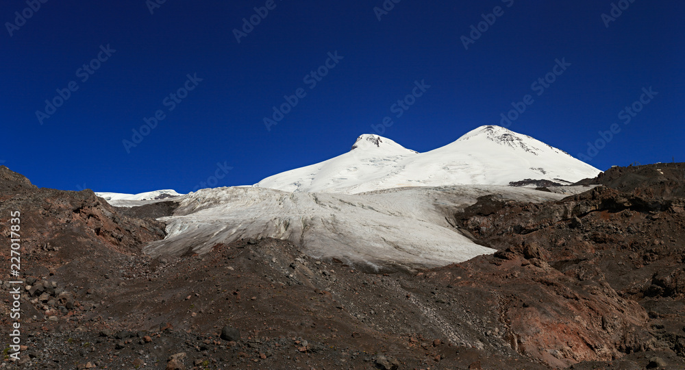 Panoramic view of the southern slope of Mount Elbrus and the Small Azau Glacier of the Caucasus Mountains in Russia. Snow-covered mountain two peaks.