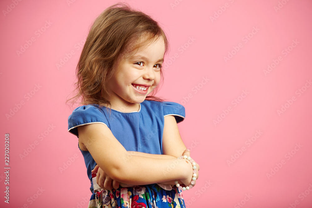 Children's beautiful girl with shyness stands on pink isolated background, wears fashionable dress of blue color. Children's beautiful girl with shyness stands on pink isolated background, wears fashionable dress of blue color.