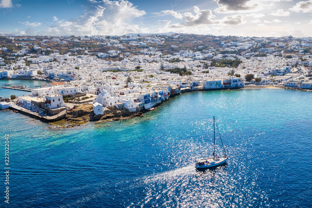 Die Bucht von Mykonos Stadt in Griechenland mit tiefblauem Meer und vorbeifahrendem Segelboot; Luftaufnahme