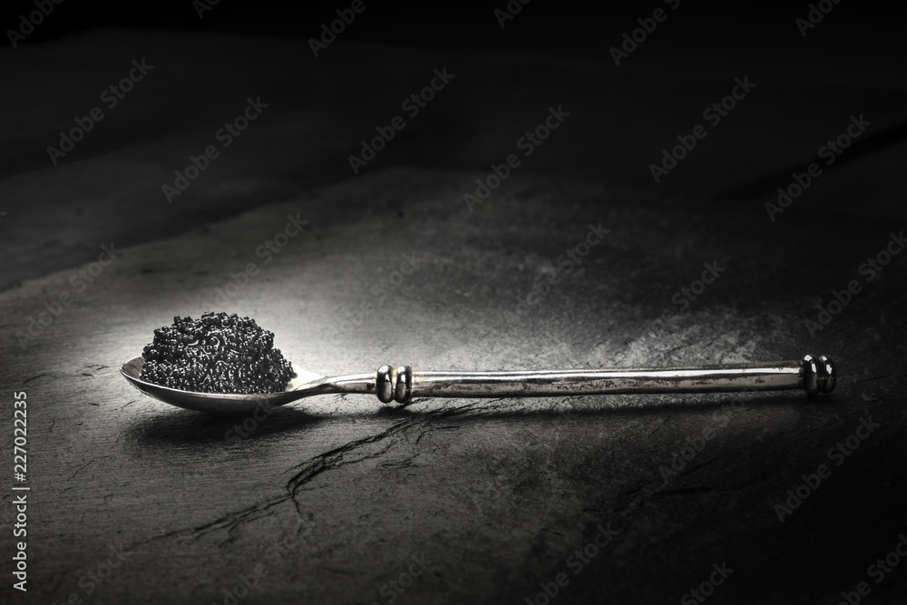 Φωτογραφία A photo of black caviar in a spoon, on a black background with copyspace