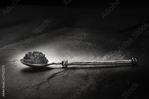 A photo of black caviar in a spoon, on a black background with copyspace