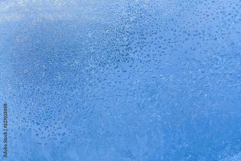 Blue frozen window glass with icy drawing with fine structure as backgroundr.