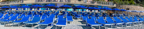 Panoramic view of blue chairs and parasol on the beach of Monterosso Al Mare village Italy