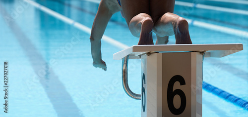 Female swimmer jumps off starting block and start swims in pool