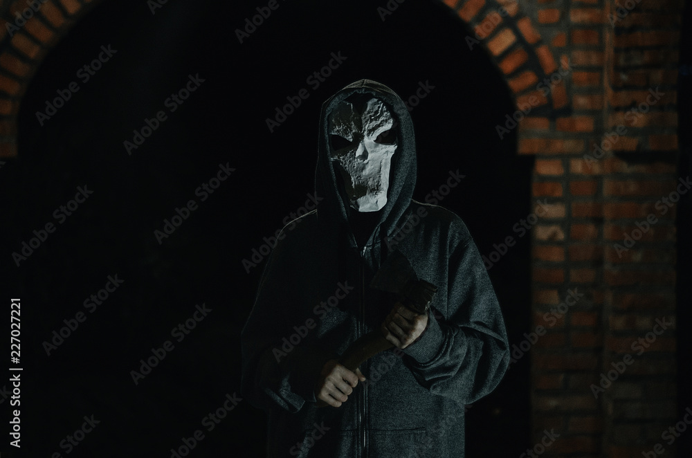 man in a hood and skull mask with a big machete on a black background man in a hood and skull mask with a big machete on a black background