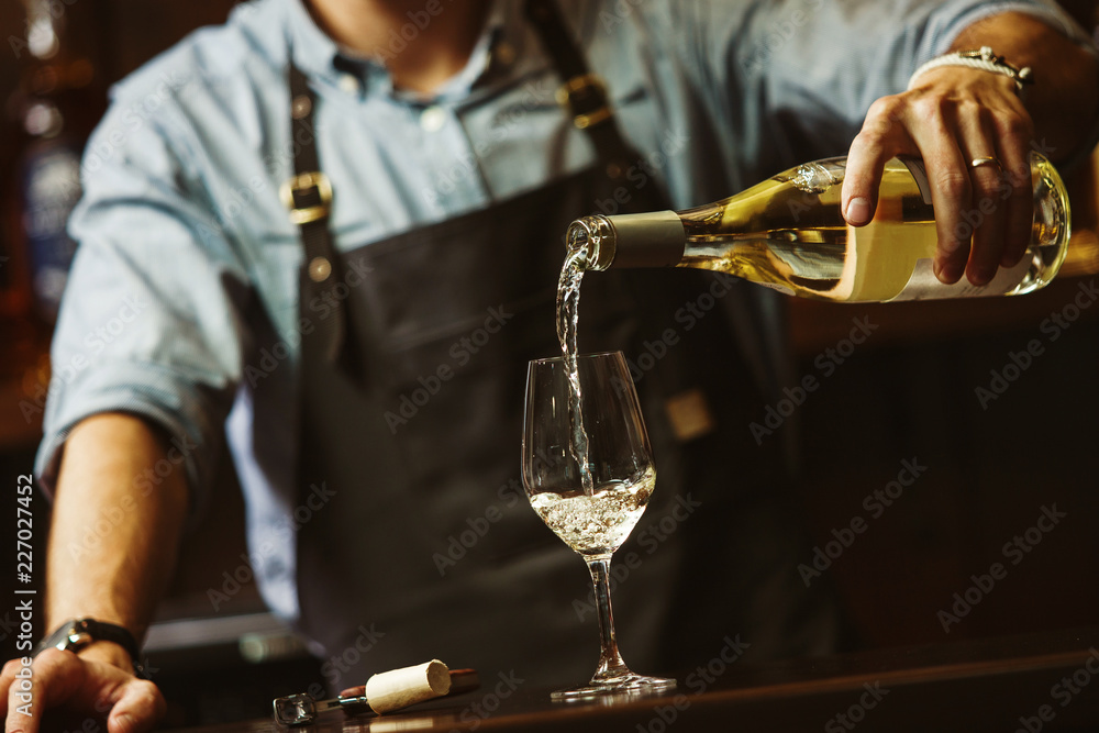 Φωτογραφία Male sommelier pouring white wine into long-stemmed wineglasses.