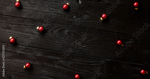 From above shot of tiny red Christmas beads lying on surface of dark timber tabletop