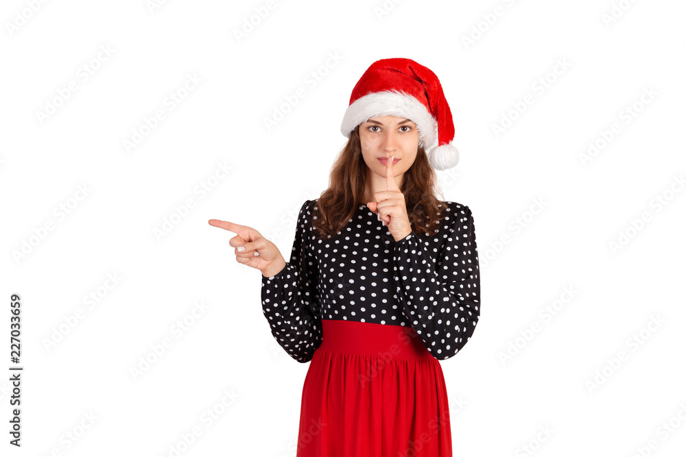 Young woman in dress pointing something with smile. emotional girl in santa claus christmas hat isolated on white background. holiday concept Young woman in dress pointing something with smile. emotional girl in santa claus christmas hat isolated on white background. holiday concept